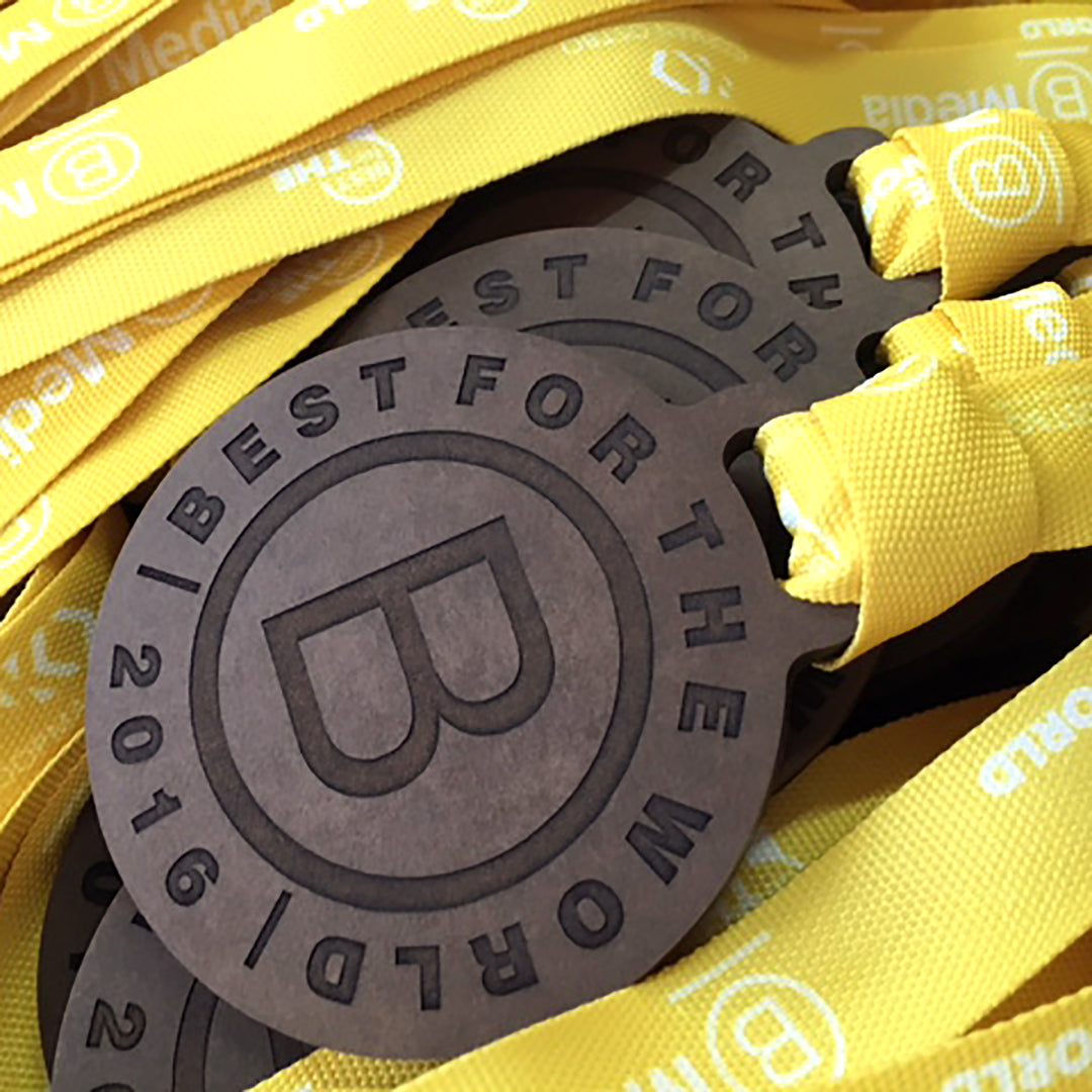 Close-up of Best for the World B Corp medals with yellow lanyards, engraved in FSC-certified recycled Richlite.