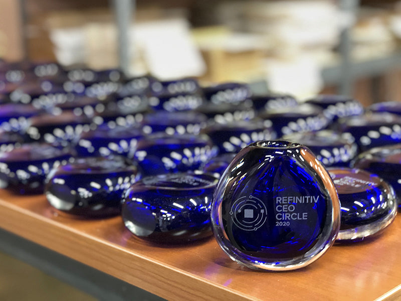 Close-up of handcrafted blue glass awards with custom etching, arranged on a wood surface.