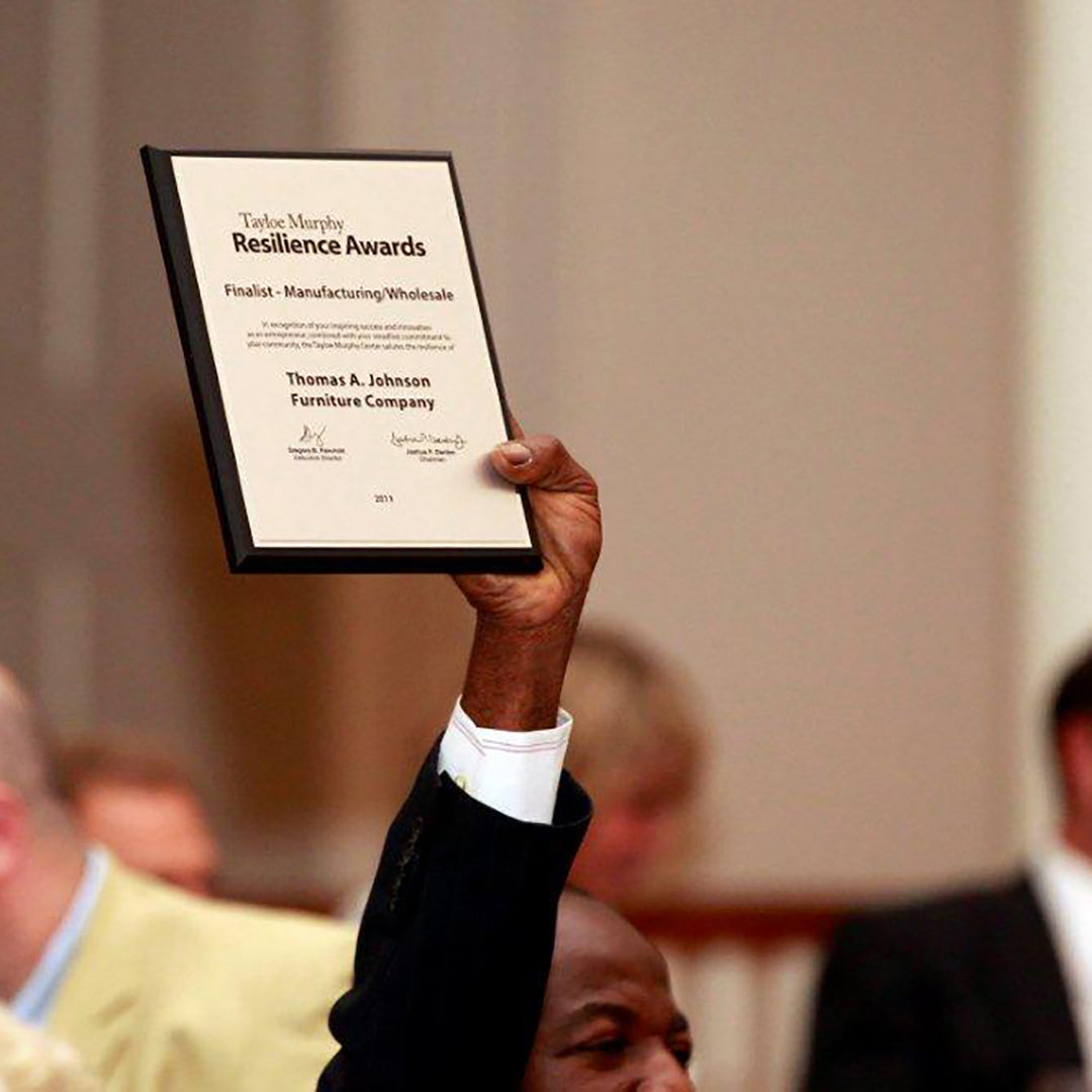 An award recipient raises a recognition plaque overhead during an awards ceremony.