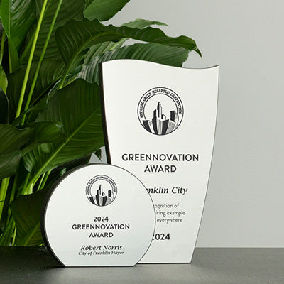Black freestanding awards made from FSC recycled materials. Both awards have silver front plates. The tall award has a wavy top. The short award is a standing circle.