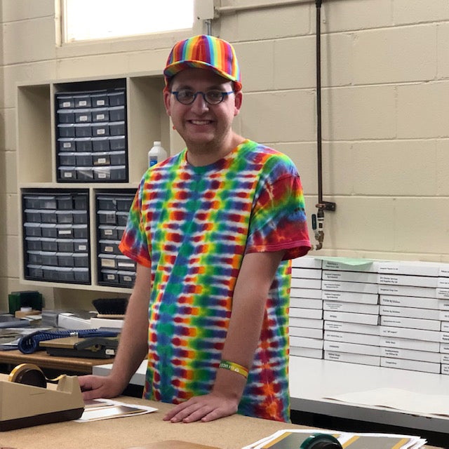 A Rivanna team member in a tie-dye shirt smiles in the production area, surrounded by finished awards.